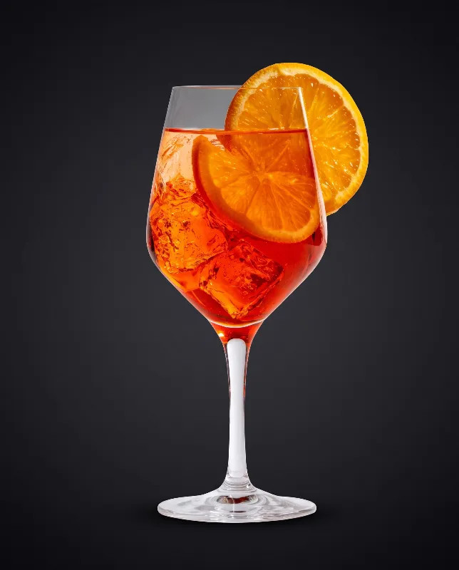 Aperol Spritz im Weinglas mit Orangenscheibe vor dunklem Hintergrund