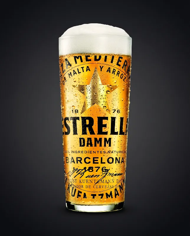 Estrella Damm Bierglas mit goldenem Bier und Aufschrift Barcelona vor dunklem Hintergrund
