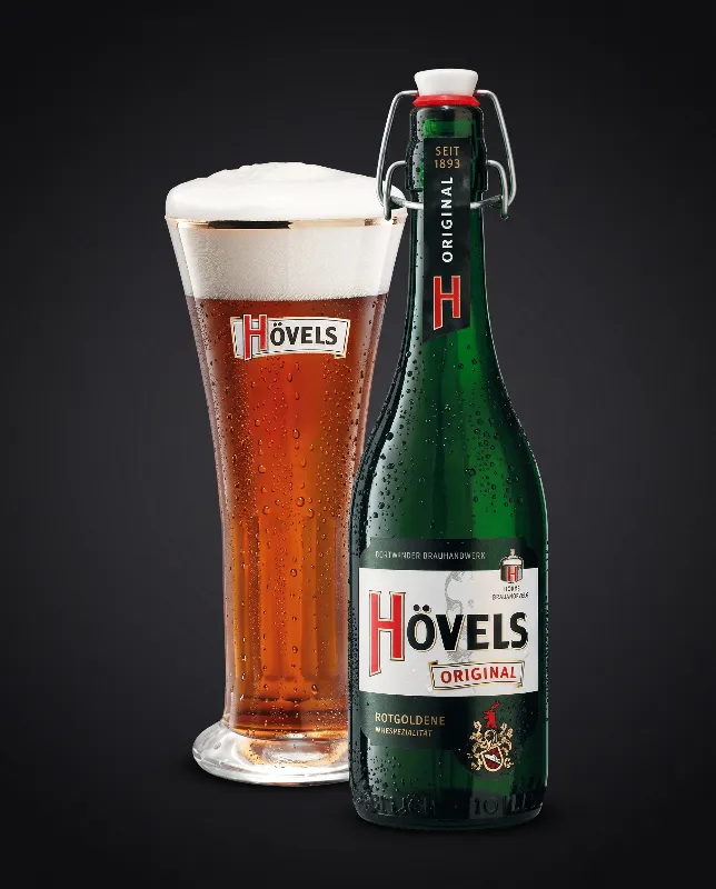 Hövels Bierflasche mit Glas, im Glas rötlich-goldenes Bier, vor dunklem Hintergrund